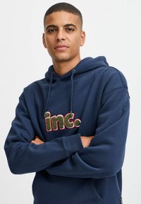Felpa blu navy con cappuccio regolabile, caratterizzata da un logo ricamato multi-colore "inc." sul davanti. Morbido al tatto, con polsini a costine.