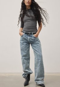 Gråtopp med kort ärm som sitter åtsittande, i kombination med ljusblå vida jeans som har ett urblekt mönster och ett svart bälte; modellen bär svarta ankelstövlar.