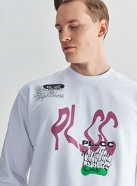 Biały sweter z grafikom w różowym i czarnym kolorze. Akcenty obejmują tekst "PL_C" w pogrubieniu, z teksturowanym zielonym detalem.