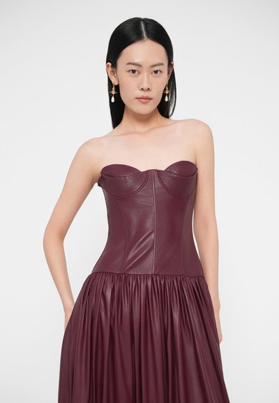 Bordové kožené šaty bez ramienok s priliehavým živôtikom s oblými švami a objemnou plisovanou sukňou. Hladká, štruktúrovaná textúra.