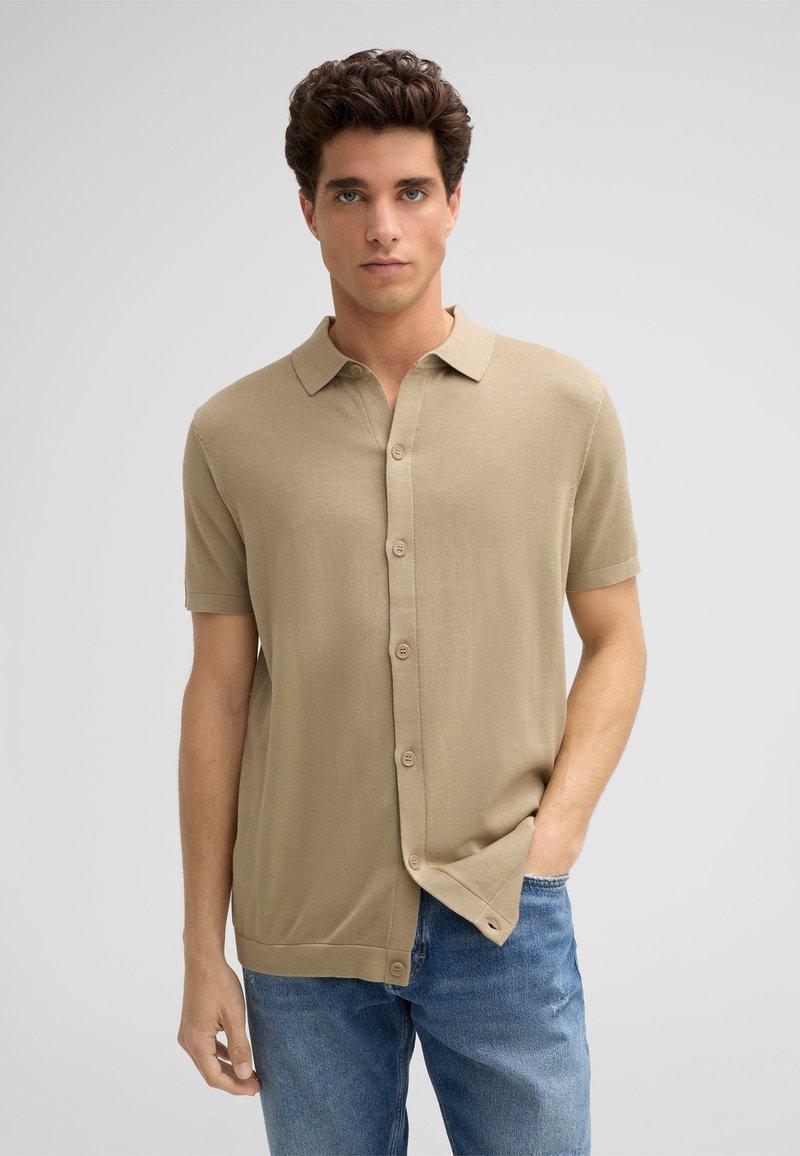 Beige korte mouwen overhemd met knopen en een spread collar, voorzien van een zachte textuur en gladde afwerking, gecombineerd met blauwe spijkerbroeken.