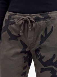 Taljeområde af mørke camouflagebukser med bundet snøre, båret med en sort ribbet top.