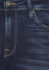 Jeans de mezclilla azul oscuro con un diseño clásico de cinco bolsillos, cierre de botón plateado, costuras en contraste y una textura suave.