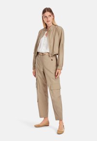 Beige Jacke mit Druckknopfverschluss, kombiniert mit beigen Cargo-Hosen mit Seitentaschen. Dazu werden hellbraune, strukturierte Ballerinas getragen.