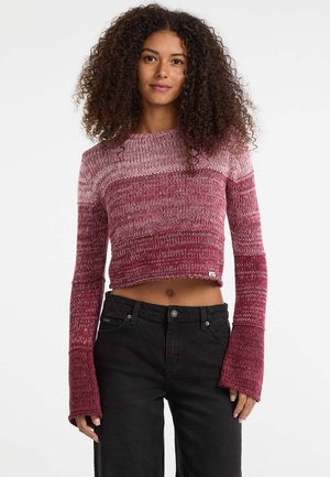 Gekruist sweater in gradient tinten van rood, met een textuur breisel, lange klokmouwen en een ronde hals; gecombineerd met zwarte broek.