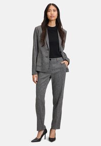 Szary teksturowany garnitur z dopasowanym żakietem i skrojonymi spodniami, w połączeniu z czarną bluzką. Charakteryzuje się gładkimi czarnymi czubkami na wysokim obcasie.