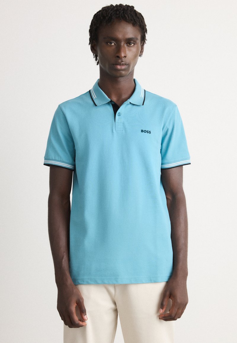 Ανοιχτό μπλε polo φανελάκι από βαμβάκι, με μαύρο γιακά, πλαισιωμένο από τρία κουμπιά και ριγέ λεπτομέρειες στα μανίκια. Εμφανές το λογότυπο "BOSS".