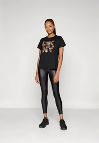 Juoda marškinėliai su leopardų raštų dizainu, trumpomis rankovėmis, derinami su blizgiomis juodomis tamprėmis ir juodais sportbačiais. Paprastas, kasdienis sportiškas įvaizdis.