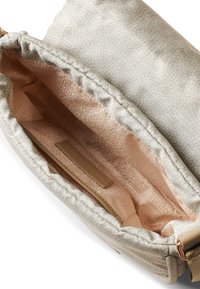 Textured beige fabric bag interior, featuring a soft, patterned lining. Includes a side pocket with a small label.