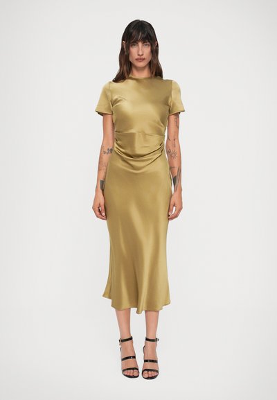 Olivgrünes Satin-Kleid mit kurzen Ärmeln, drapierten Details an der Taille und einem dezent ausgestellten Saum, kombiniert mit schwarzen Riemchensandalen.