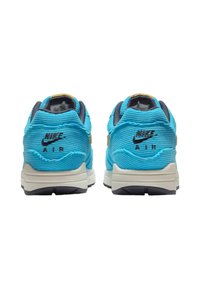 Nike Air sneakers feature a textured blue upper, beige accents, and a white midsole. The design includes a visible logo on the heel.