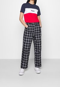 Rood, wit en marineblauw gekleurde color-block T-shirt met het "FILA" logo, gecombineerd met zwart-wit geruite hoge taille broeken en witte sneakers.