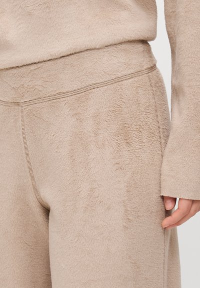 Beige fleece loungewear with a soft, textured finish. Features elastic waistband and stitched seam details. Slightly relaxed fit.