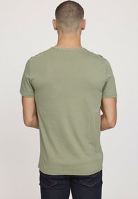 T-shirt en coton vert à manches courtes avec un col rond, texture lisse et coupe décontractée, vu de dos avec un jean bleu foncé.