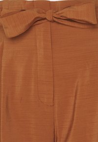 Tkanina w kolorze rdzy o fakturowanej, prążkowanej powierzchni. Zawiązywana kokarda w talii oraz detal z szwem z przodu.