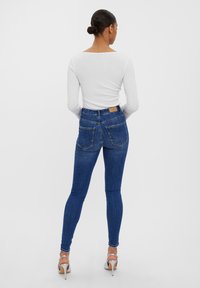 Blå högmidjade smala jeans i denim med en slät textur, med två bakfickor och en brun läderlapp vid midjan.