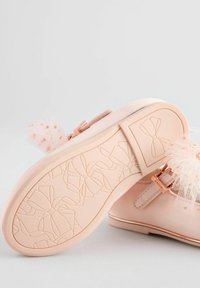 Scarpa rosa pallido con tomaia in tessuto strutturato e dettaglio in tulle a fiocco. Presenta una suola in gomma decorata con motivi a fiocco e un accento in oro rosa.
