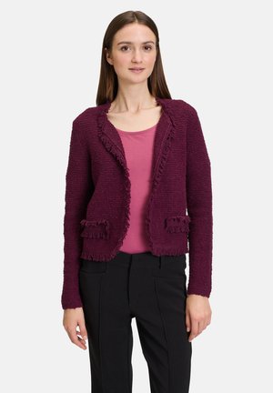 Burgundy textured jacket with frayed edges, features two front pockets and a collarless design, paired with a pink top and black trousers.