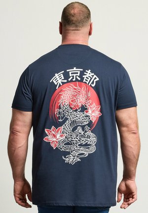 Mand set bagfra iført navyblå skjorte med hvid drage og rød cirkeldesign og japanske tegn over dragen.