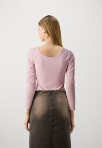 Roza majica dugih rukava s zaobljenim izrezom, u kombinaciji s smešnom traper suknjom koja ima vidljivi zip na stražnjoj strani i prilagođen siluet.
