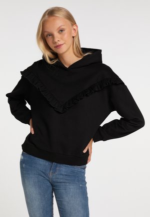 Felpa nera con cappuccio e un design arricciato sul petto. Il materiale sembra morbido ed è abbinata a jeans blu.