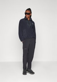 Zwarte fleece pullover met kwart rits en hoge kraag, gecombineerd met zwarte cargo pants met ritszakken en zwarte wandelschoenen.