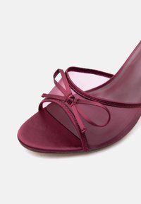 Ανοιχτή μωβ ψηλοτάκουνα γόβα με διάφανο πλέγμα στην επάνω πλευρά και λεπτομέρεια με σατέν φιόγκο σε λευκό φόντο.