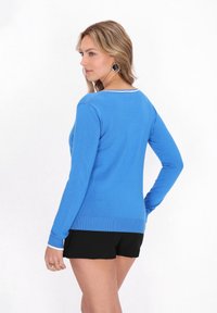 Blauer Strickpullover mit Rundhalsausschnitt und gerippten Bündchen, kombiniert mit schwarzen Shorts. Verfügt über eine glatte Textur und einen weißen Akzent am Ausschnitt.
