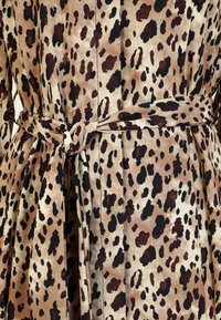 Robe en tissu imprimé léopard avec des nuances de beige, marron et noir. Dispose d'une taille nouée et de détails plissés. Texture lisse, design élégant.