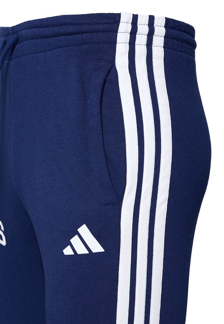 Granatowe dresy z białymi paskami po bokach, wykonane z miękkiego materiału. Posiadają elastyczny pas i boczną kieszeń. Widoczne logo Adidas.