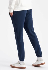 Marinblå joggers med elastiska mudd, sidofickor och en avslappnad passform, i kombination med vita sneakers och texturerade ankelsockor.