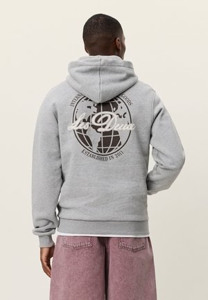 Sudadera con capucha gris con un gráfico de globo en la espalda, con el texto "Les Deux" y "Establecido en 2011" en blanco contrastante.