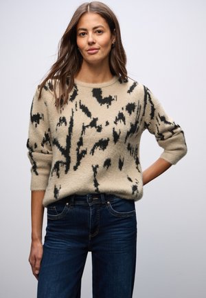 Maglione beige con motivo astratto nero, tessuto misto lana, scollo rotondo e maniche a 3/4, abbinato a jeans blu scuro.