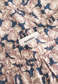 Blomstret stof med magnolia-lignende blomster i blå og creme med brune konturer. Elastisk taljebånd med en synlig mærkelabel "GABBA."
