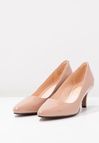 Escarpins en cuir verni nude avec des bouts pointus, des talons bas, une texture lisse et un design minimaliste. Caractéristiques d'une couleur unie sans motifs.