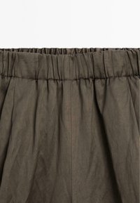 Elastische tailleband in een donkergroene stof, met een geplooide textuur en zachte afwerking. Ontworpen voor een comfortabele pasvorm en bewegingsgemak.