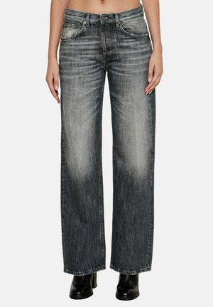 Jeans neri sbiaditi a gamba larga indossati con stivali neri con tacco, che mostrano dalla vita ai piedi una persona con addome scoperto su sfondo bianco.