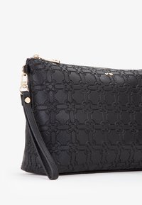 Zwarte leren clutch met een gegraveerd bloemenpatroon, gouden hardware, ritsluiting en afneembare polsband. Gladde textuur.
