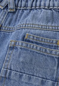 Ljusblå denimtyg med synlig sömnad. Har ett rynkat midjeband och två bakfickor. Texturen är slät med ett klassiskt jeansmönster.