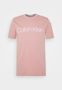 Różowa bawełniana koszulka z krótkim rękawem. Posiada biały nadruk logo "Calvin Klein" na przodzie. Okrągły dekolt i gładka faktura.