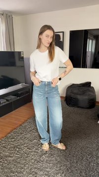 Lichtblauwe wijdvallende spijkerbroek van denim, gecombineerd met een eenvoudig wit T-shirt. De omgeving bevat een donkere televisie en een zacht zitzak.