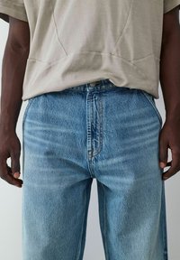 Camiseta de color beige claro con un corte relajado, combinada con jeans de mezclilla azul claro, desgastados, de corte recto y costuras visibles.