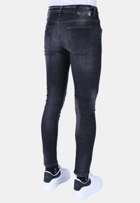 Zwarte skinny jeans met een vervaagde textuur, met een klassieke vijf-pocketontwerp en een leren taillebandlabel. Draagt met witte sneakers.