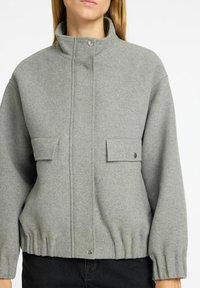 Grijze wolmix jas met een hoge kraag, een rits aan de voorkant en twee flapzakken; heeft een geraffineerde zoom en geribbelde manchetten.