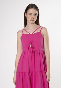 Roze jurk met dunne bandjes, voorste strikdetail en gerimpelde lagen. Soepele textuur met een relaxte pasvorm. Eenvoudig en casual ontwerp.