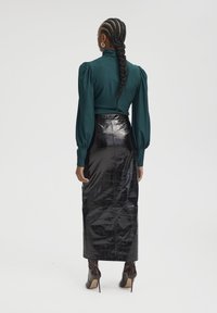 Femme aux longs cheveux tressés portant un haut bleu sarcelle à manches bouffantes, une jupe midi texturée noire et des bottines à talons hauts marron foncé, de dos.