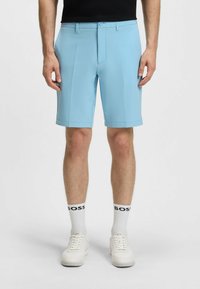 Pantaloni corti azzurri realizzati in tessuto liscio, dotati di una parte anteriore piatta, passanti per cintura e orlo rifinito. Indossati con scarpe bianche e calze con logo.