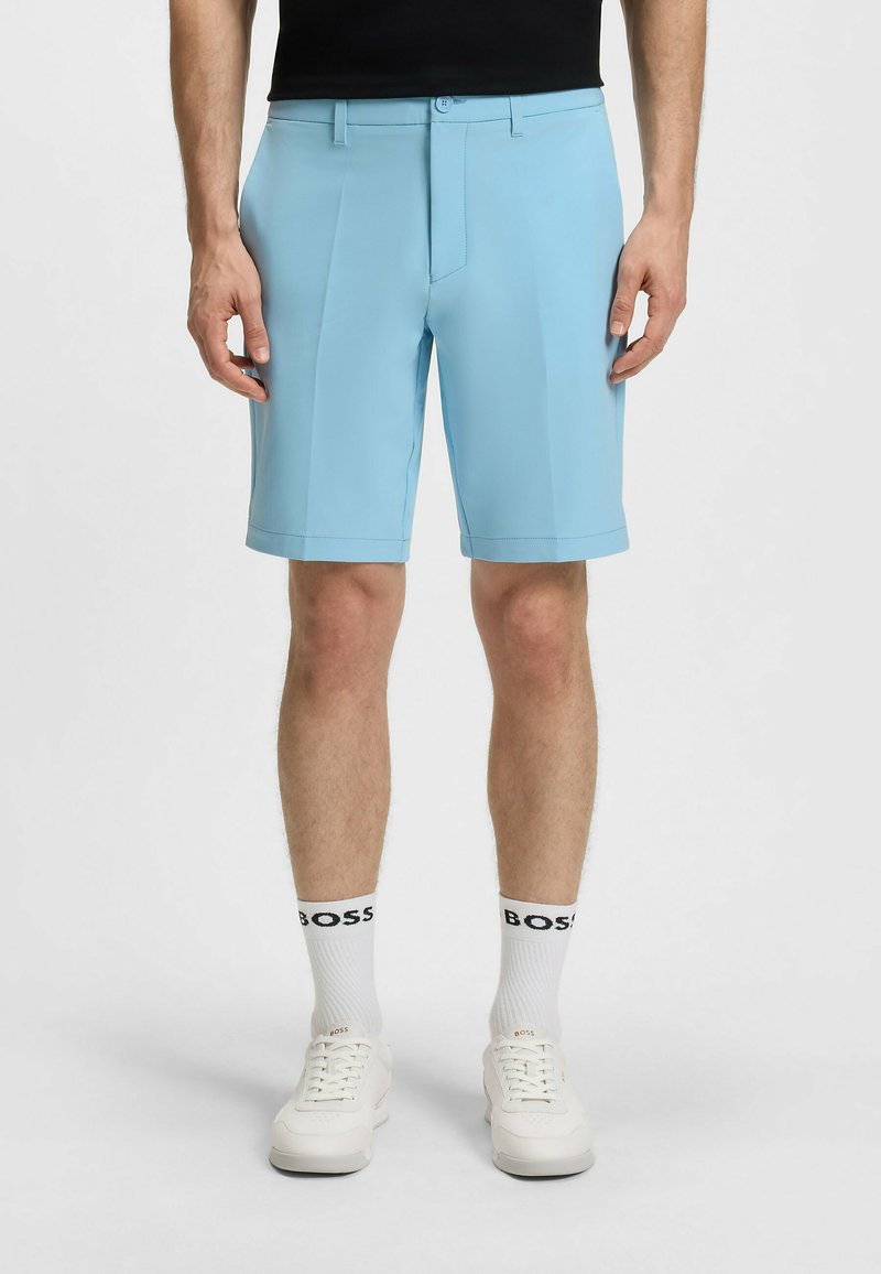 Pantaloni corti azzurri realizzati in tessuto liscio, dotati di una parte anteriore piatta, passanti per cintura e orlo rifinito. Indossati con scarpe bianche e calze con logo.
