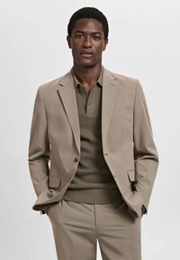 Beige suit with a tailored fit, featuring a single-button blazer and a textured olive green polo. Smooth fabric, minimal detailing.