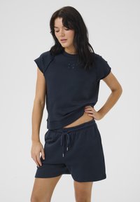 Sweatshirt din bumbac de culoare bleumarin, cu mâneci scurte și gât rotund, potrivit cu pantaloni scurți asortați ce au o talie elastică și un șnur.